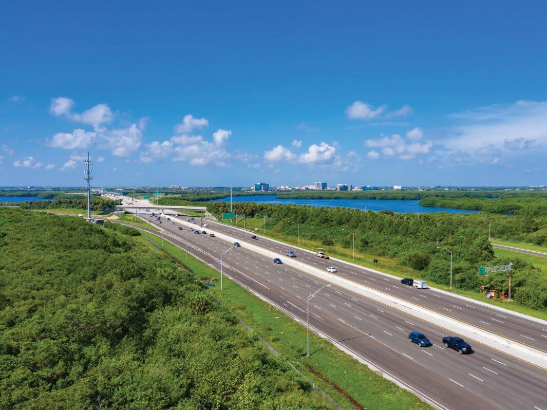 Elevated view of a multilane Interstate 275 approach running through mangroves beside Tampa Bay, with the St. Petersburg skyline on the horizon.