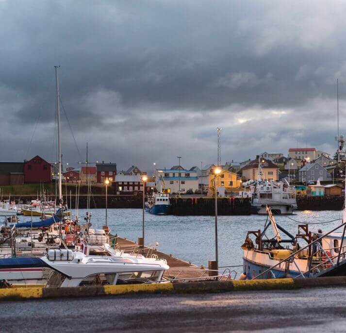Wharf at Stykkishólmur, Iceland, lined with tall black extruded rubber fenders below a steep rock cliff.