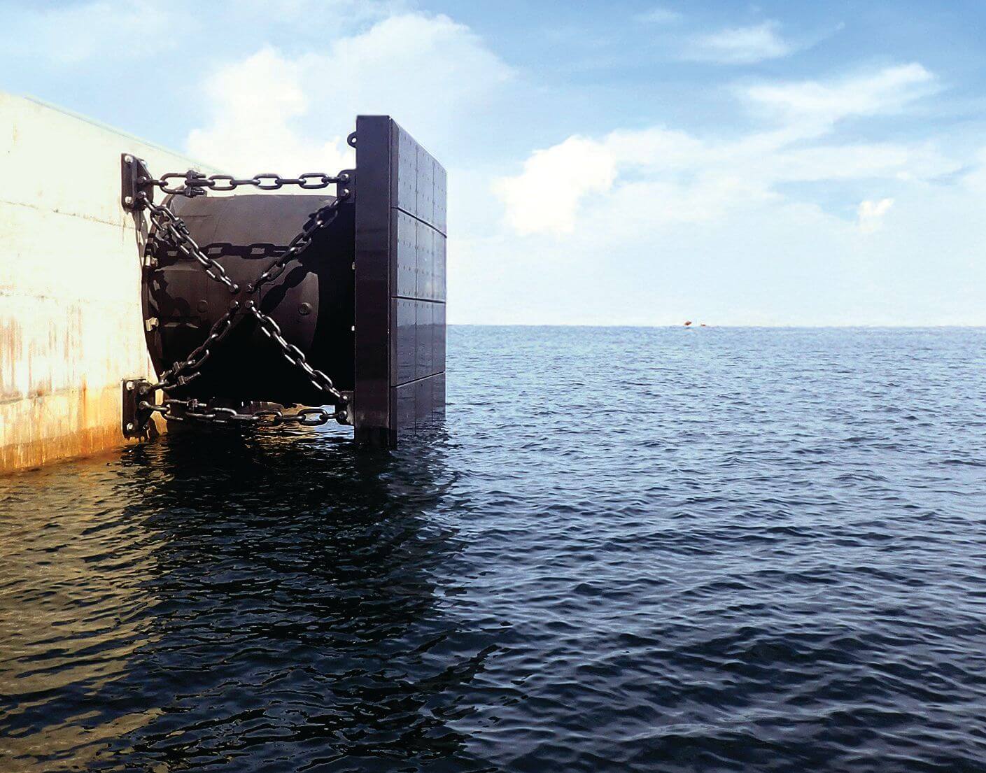 Large black cell fender with a steel panel and crossed chains mounted on a concrete berth wall above open water.