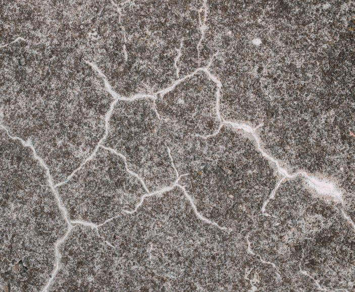 Close-up of a concrete surface crossed by a network of fine cracks filled with white material.